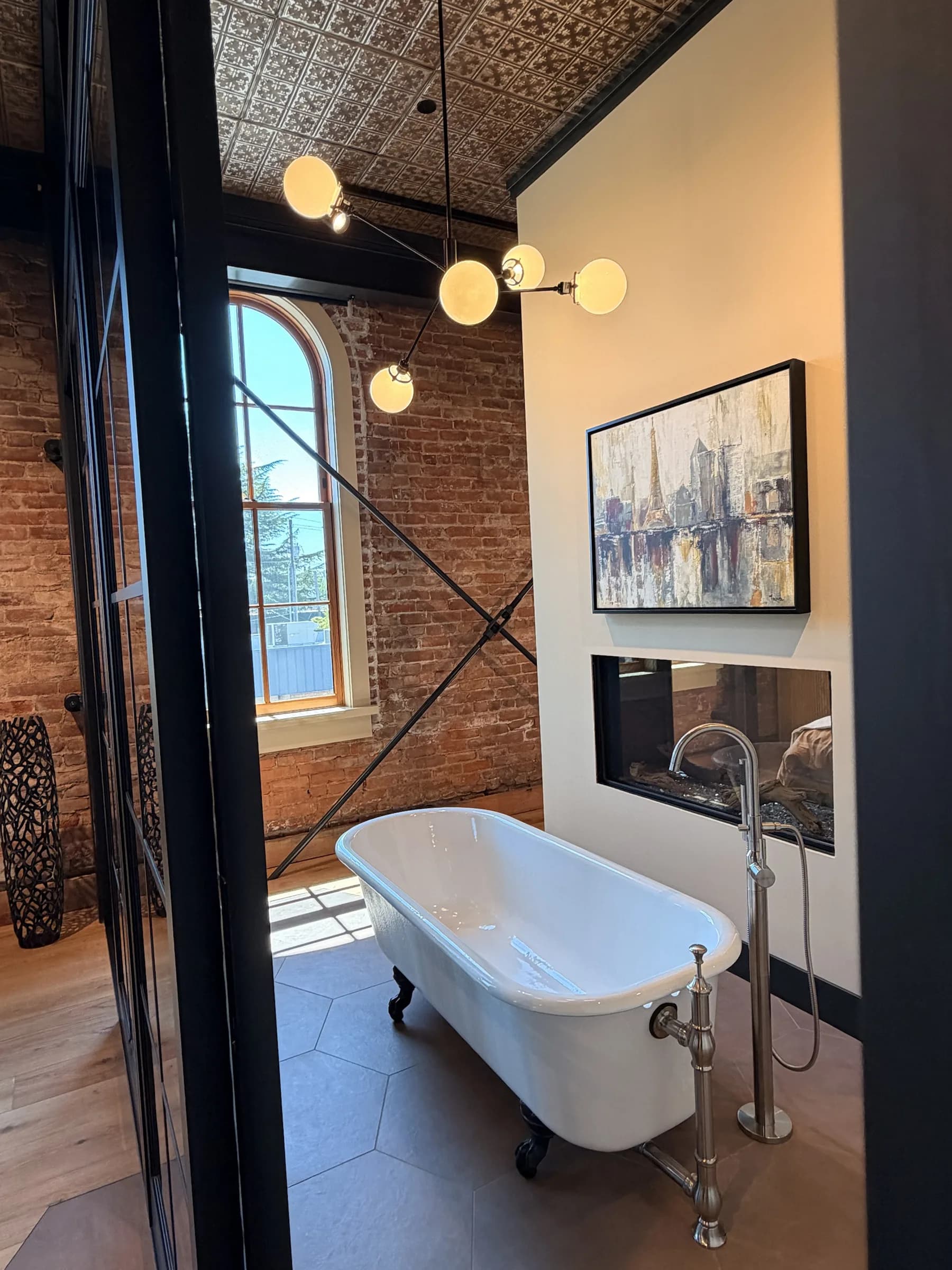 Clawfoot soaking tub beside a fireplace, exposed brick, and arched window