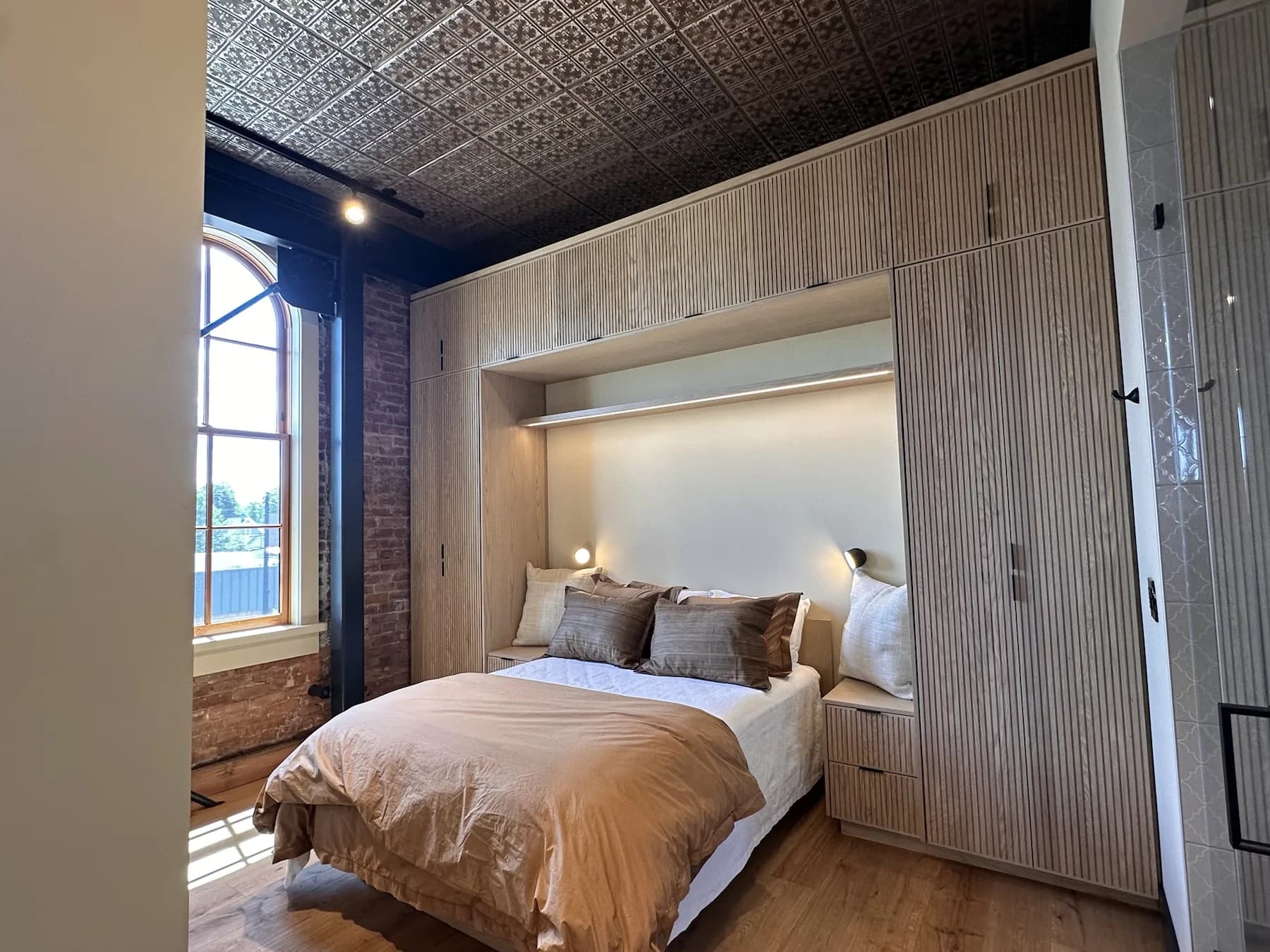 Bedroom with arched historic window, brick wall, and decorative ceiling